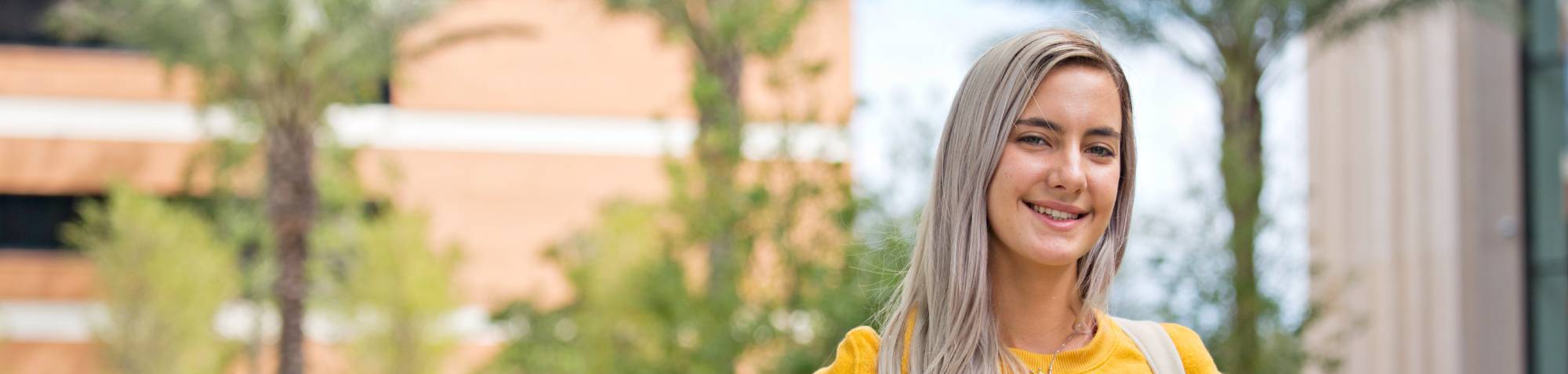 student smiling in yellow sweater with backpack