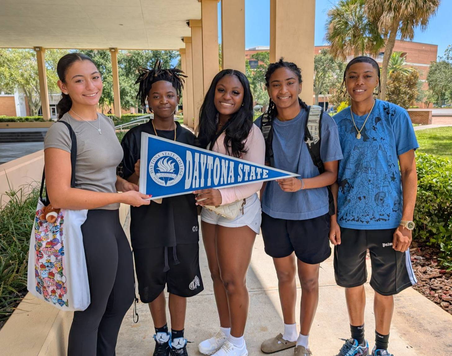 A group of students holding a Daytona State College pennant on campus.  