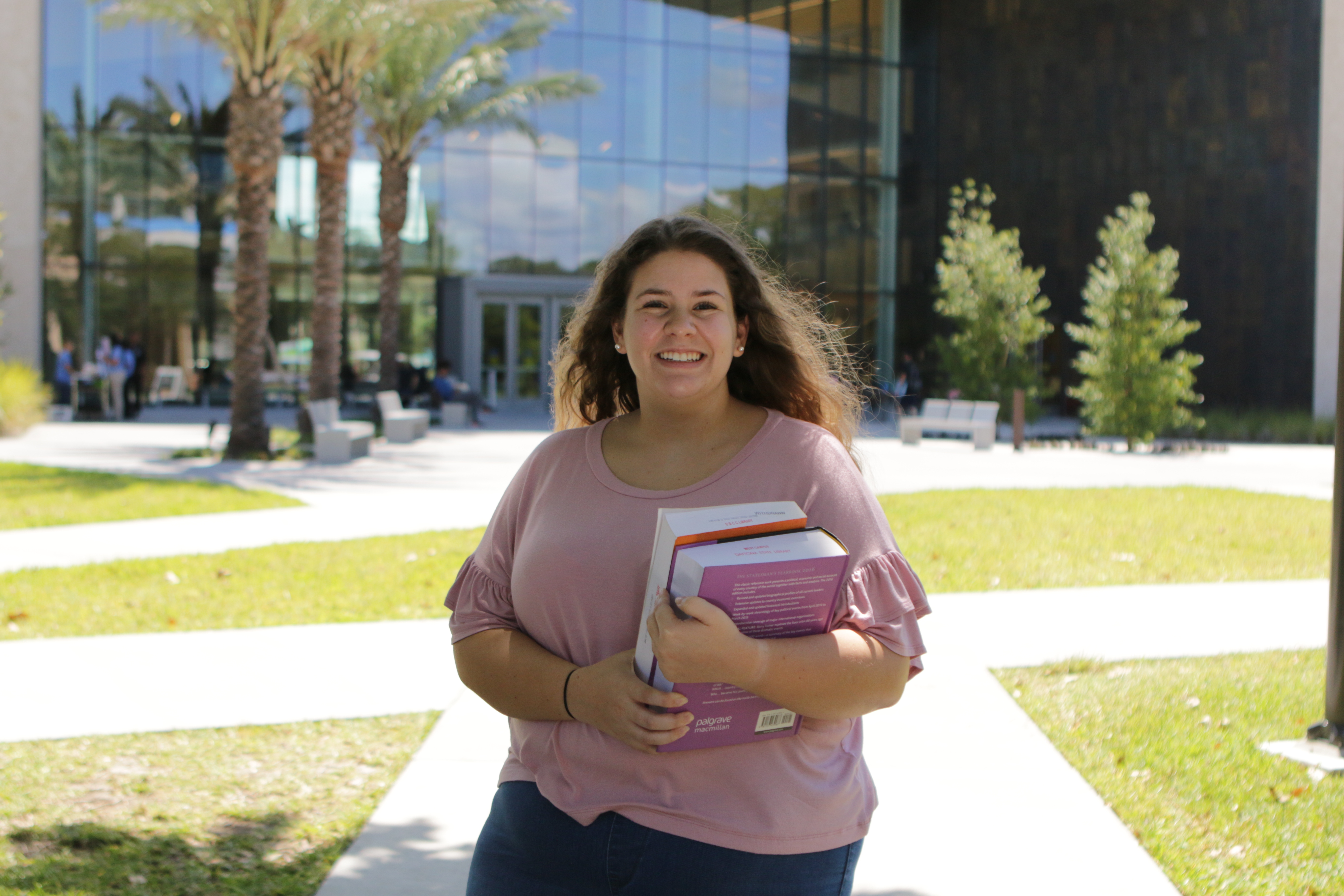 smiling student in pink shirt outside holding textbooks